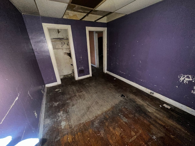 unfurnished bedroom with a drop ceiling, wood finished floors, and baseboards