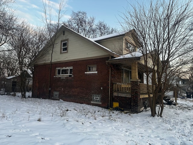 snow covered property with a porch and brick siding