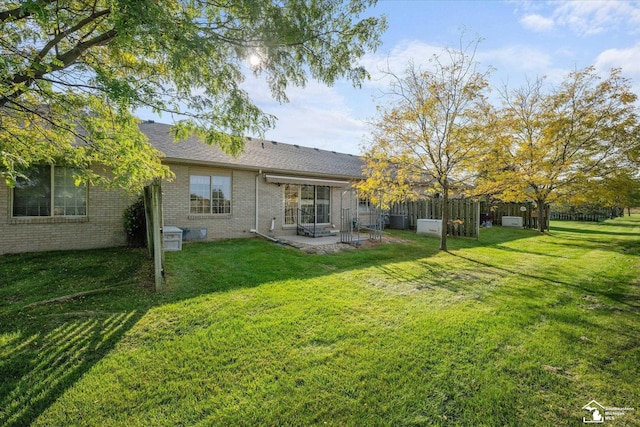 rear view of house featuring roof with shingles, fence, a yard, a patio area, and brick siding