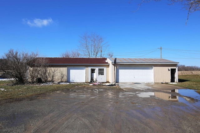 view of front facade with a garage, metal roof, driveway, and an outdoor structure