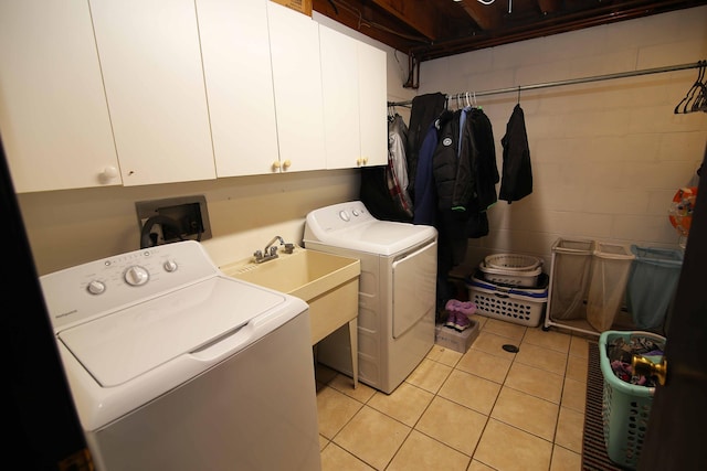 washroom with concrete block wall, washing machine and clothes dryer, cabinet space, light tile patterned flooring, and a sink