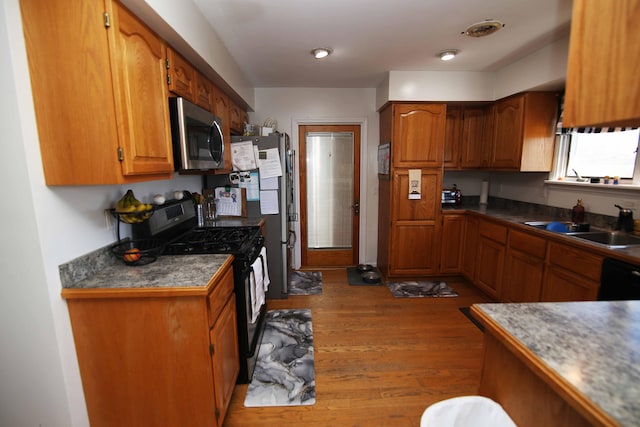 kitchen with visible vents, appliances with stainless steel finishes, brown cabinets, wood finished floors, and a sink