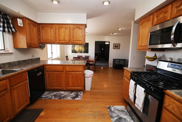 kitchen with a peninsula, appliances with stainless steel finishes, light wood-type flooring, brown cabinets, and dark countertops