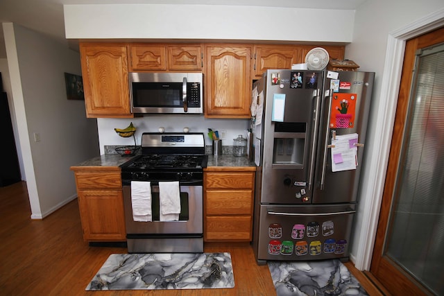 kitchen featuring appliances with stainless steel finishes, brown cabinetry, baseboards, and wood finished floors