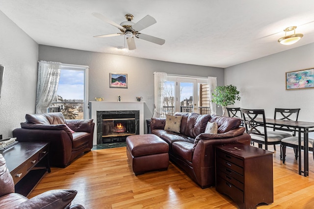 living room featuring light wood-style floors, a ceiling fan, a textured wall, and a premium fireplace