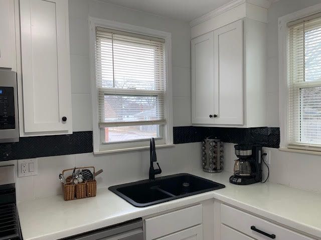 kitchen with tasteful backsplash, white cabinets, dishwasher, stainless steel microwave, and a sink