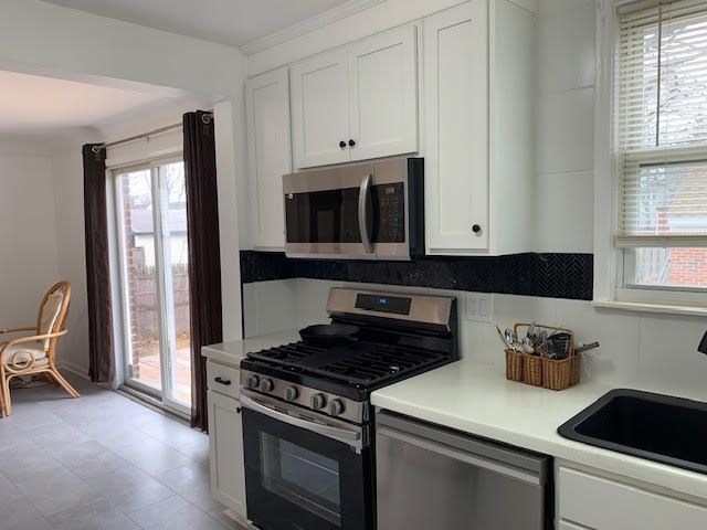 kitchen featuring white cabinets, appliances with stainless steel finishes, a sink, light countertops, and backsplash