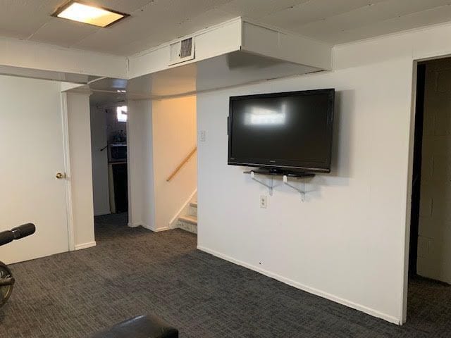 interior space with visible vents, dark carpet, stairway, and baseboards