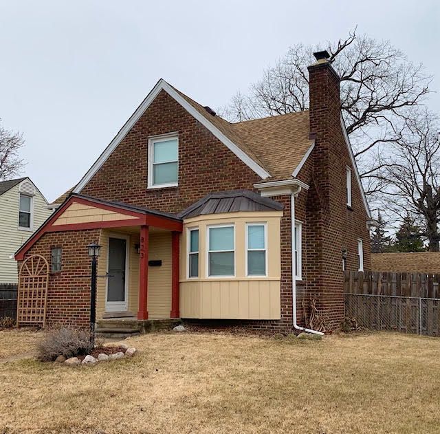 back of house with brick siding, a lawn, a chimney, and fence