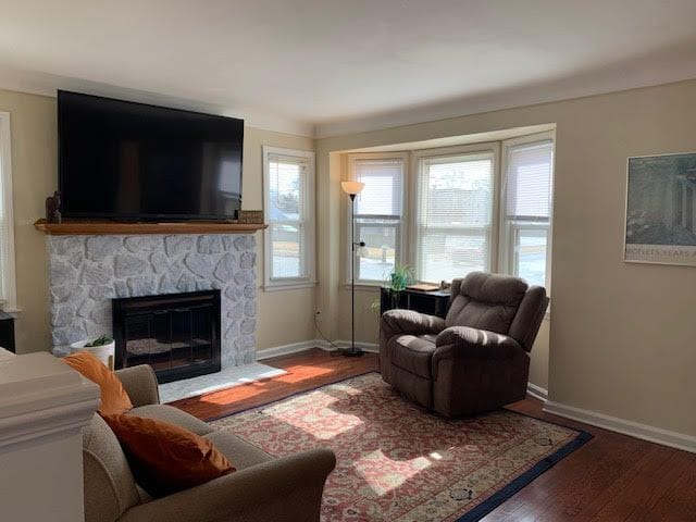 living room with a wealth of natural light, a stone fireplace, baseboards, and wood finished floors