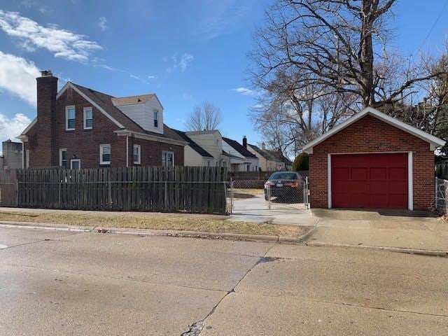 view of side of home featuring a garage, a fenced front yard, concrete driveway, and brick siding