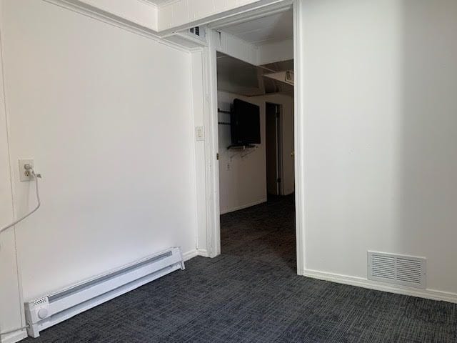 empty room with a baseboard radiator, visible vents, dark carpet, and baseboards