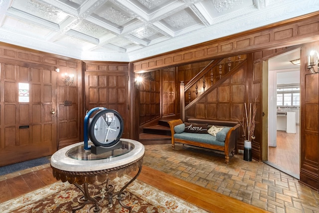 living area featuring ornamental molding, wooden walls, coffered ceiling, beamed ceiling, and stairs