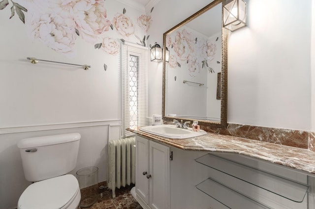 half bathroom featuring toilet, a decorative wall, vanity, radiator, and crown molding