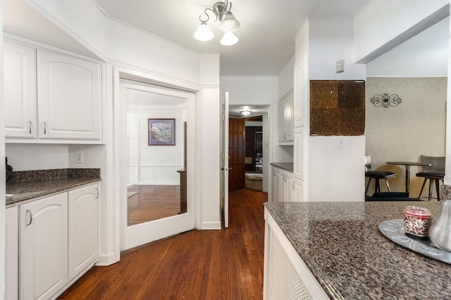 kitchen featuring dark wood-style flooring, crown molding, an inviting chandelier, white cabinets, and dark stone countertops