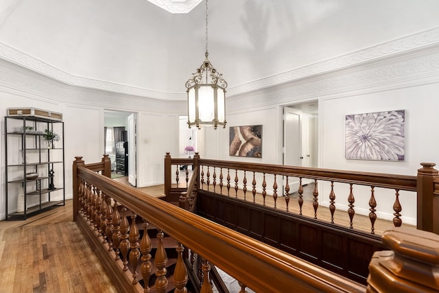 corridor with a chandelier, wood finished floors, an upstairs landing, and a decorative wall