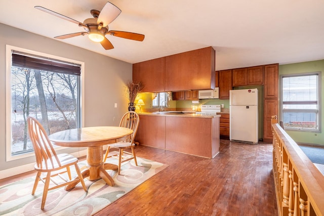 kitchen featuring a peninsula, white appliances, wood finished floors, light countertops, and brown cabinetry