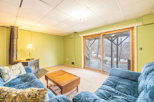 living area with carpet, a wood stove, a paneled ceiling, and baseboards