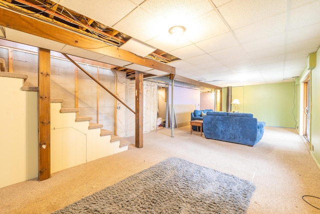 basement with stairway, a drop ceiling, and carpet flooring