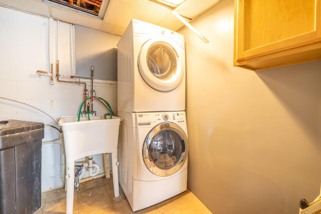 washroom featuring stacked washer / dryer, cabinet space, and concrete block wall