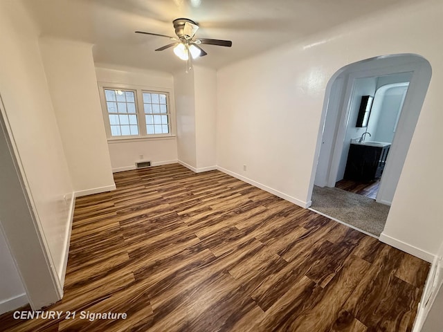 spare room with arched walkways, dark wood-style flooring, visible vents, and baseboards