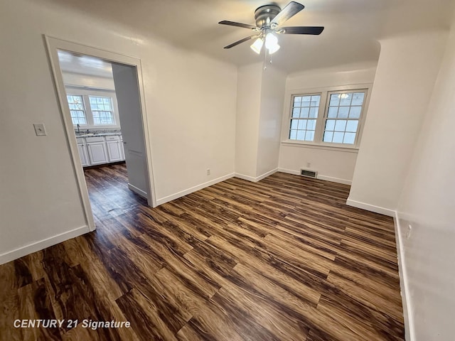 empty room with baseboards, visible vents, ceiling fan, dark wood-type flooring, and a sink