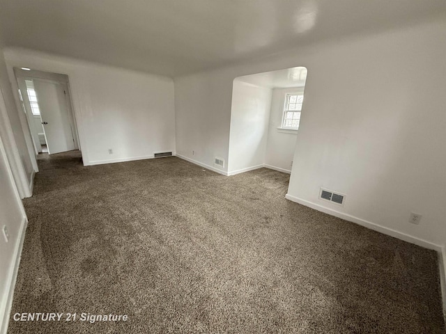 empty room featuring baseboards, visible vents, and dark carpet