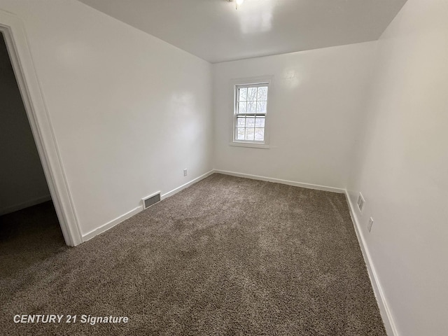 empty room featuring baseboards, visible vents, and dark carpet