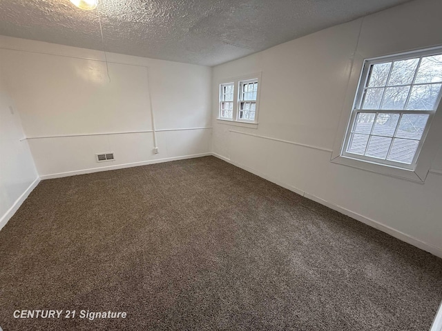 unfurnished room with dark colored carpet, visible vents, a textured ceiling, and baseboards