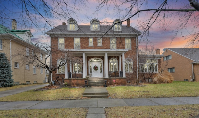 colonial inspired home featuring a yard, a chimney, a porch, and brick siding