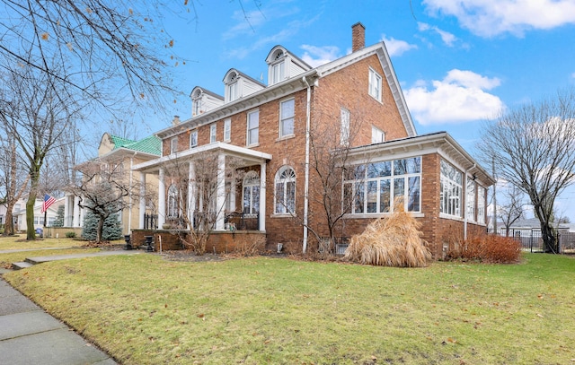 view of front of house with brick siding, a front lawn, a chimney, and fence