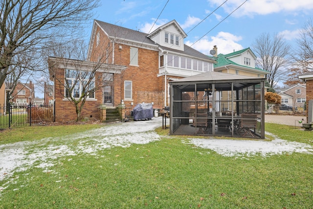 back of house featuring a sunroom, brick siding, fence, and a lawn