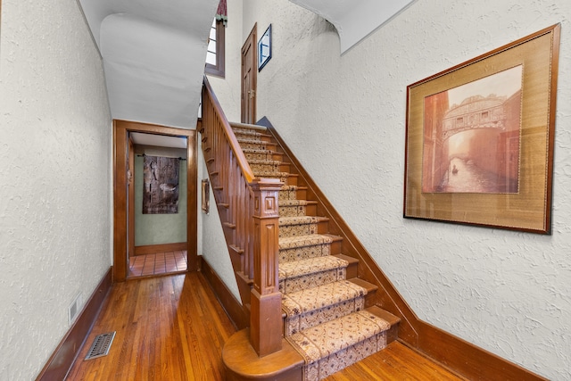 staircase with visible vents, a textured wall, and hardwood / wood-style flooring