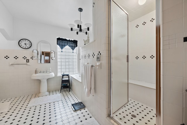 full bathroom with tile walls, a stall shower, a sink, a chandelier, and tile patterned floors