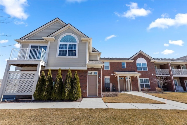 view of property featuring brick siding, a balcony, and a front yard