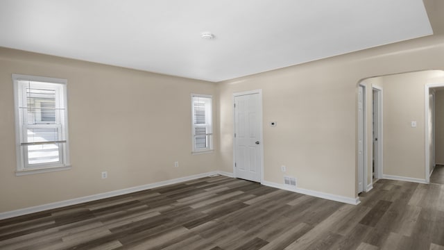 empty room with dark wood-style floors, arched walkways, visible vents, and baseboards