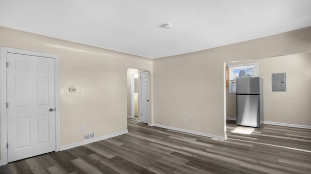 empty room with electric panel, visible vents, arched walkways, dark wood finished floors, and baseboards