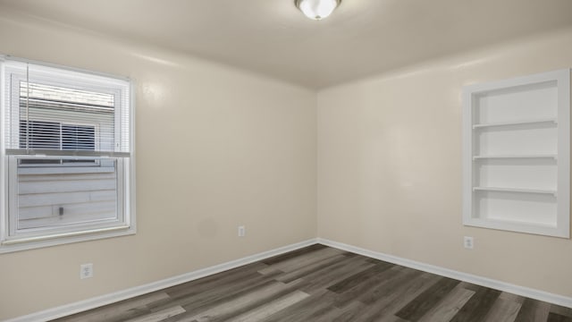 empty room featuring baseboards, built in features, and dark wood-style flooring