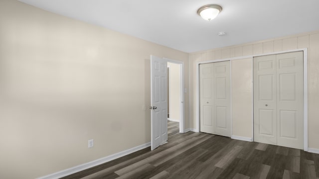 unfurnished bedroom with a closet, dark wood finished floors, and baseboards