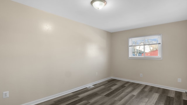 spare room with dark wood-type flooring, visible vents, and baseboards