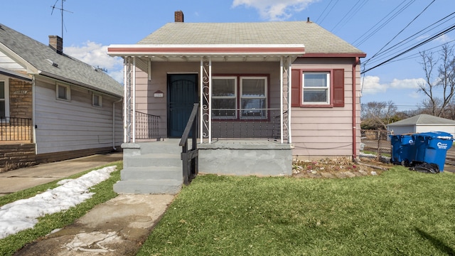 bungalow-style home featuring covered porch, roof with shingles, and a front yard