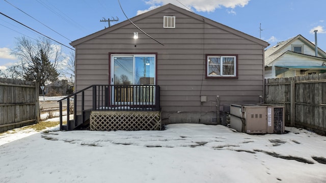 snow covered house featuring central AC unit and fence