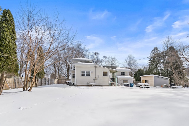 snow covered back of property with an outbuilding, fence, and a garage