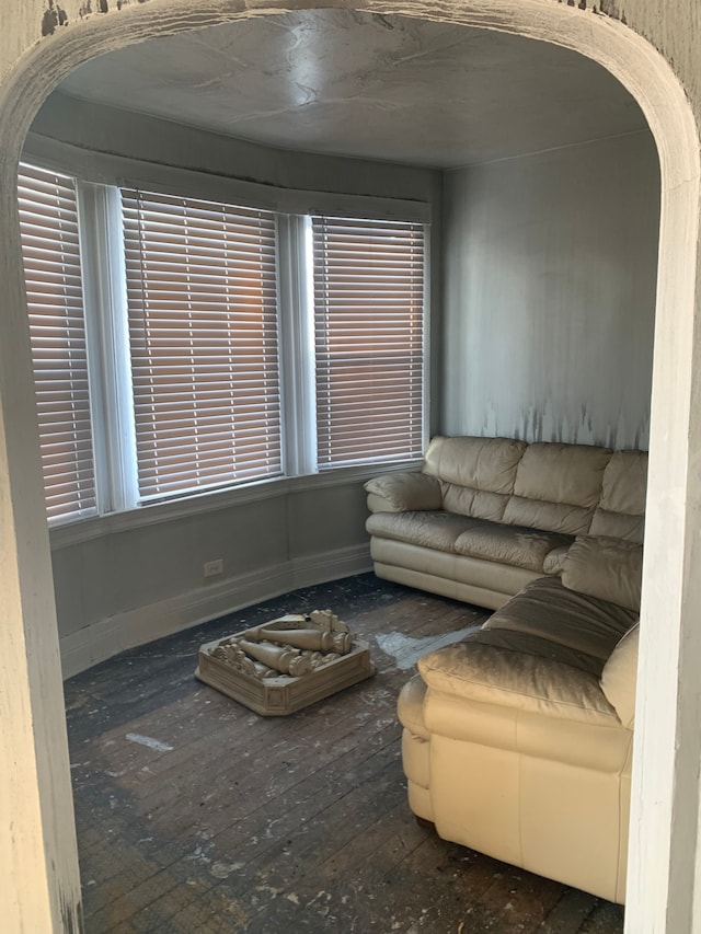 unfurnished living room featuring arched walkways, hardwood / wood-style flooring, and baseboards