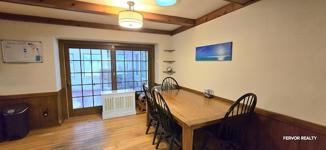 dining area with light wood-type flooring, beam ceiling, a wainscoted wall, and wood walls