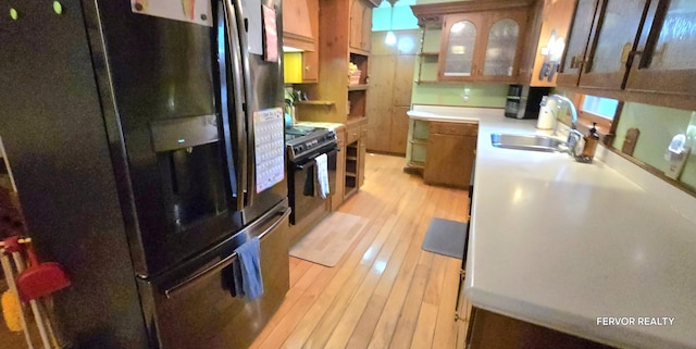 kitchen with brown cabinets, light countertops, light wood-type flooring, black appliances, and a sink