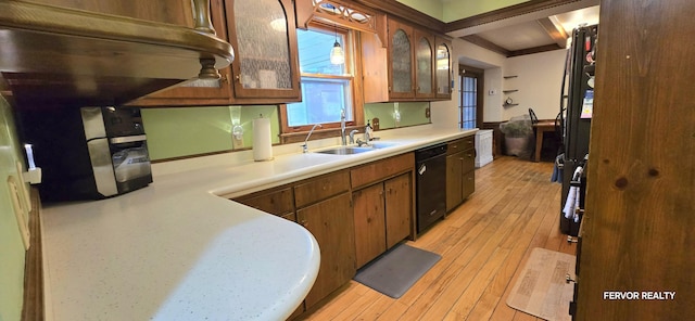 kitchen featuring a sink, black dishwasher, light countertops, light wood-type flooring, and glass insert cabinets