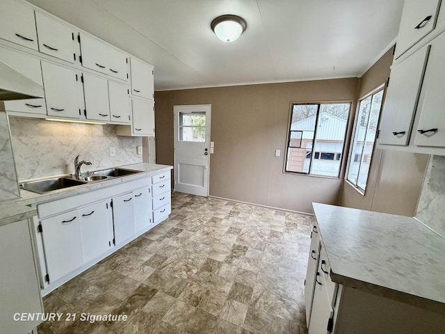 kitchen with tasteful backsplash, stone finish flooring, light countertops, white cabinetry, and a sink