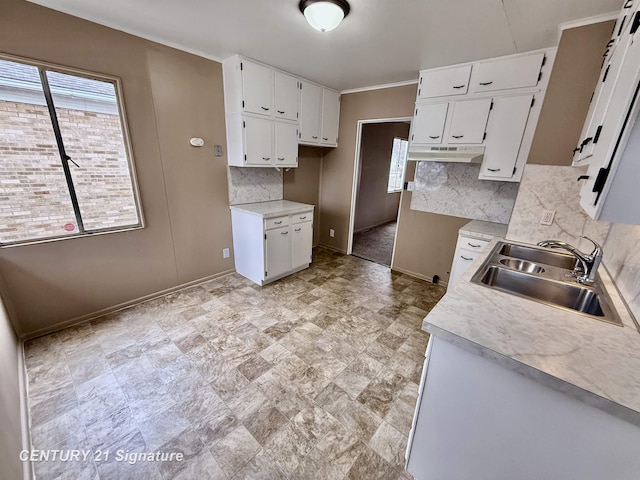 kitchen featuring under cabinet range hood, backsplash, white cabinets, and a sink