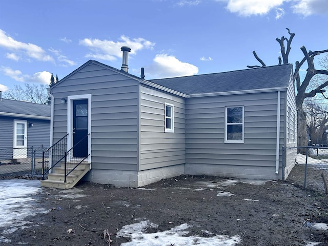 rear view of property featuring entry steps, fence, and roof with shingles